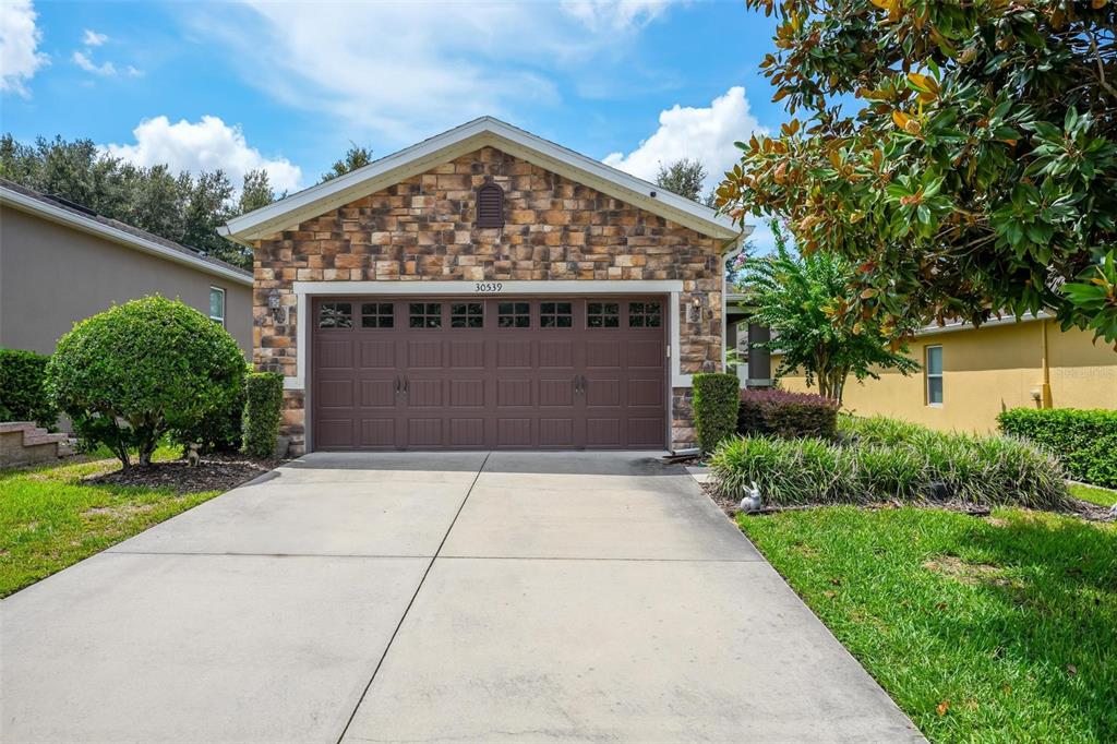 A single-story house features a stone facade, a brown two-car garage, and a concrete driveway — 30539 LIPIZZAN TERRACE, MOUNT DORA, FL