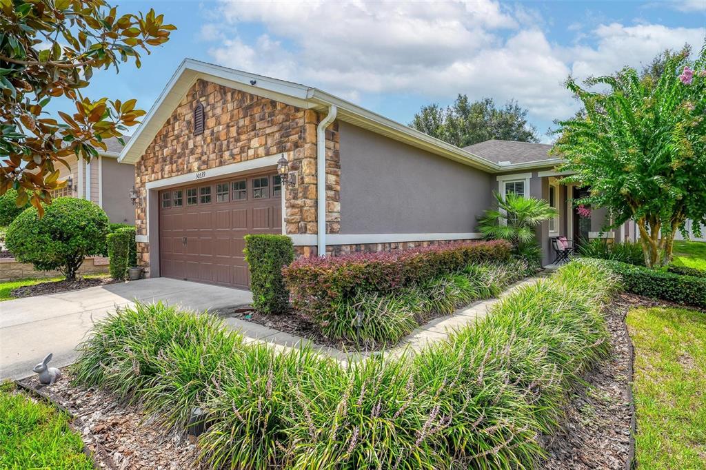 A single-story house features a stone-accented garage, a concrete driveway, and landscaped front yard beds — 30539 LIPIZZAN TERRACE, MOUNT DORA, FL