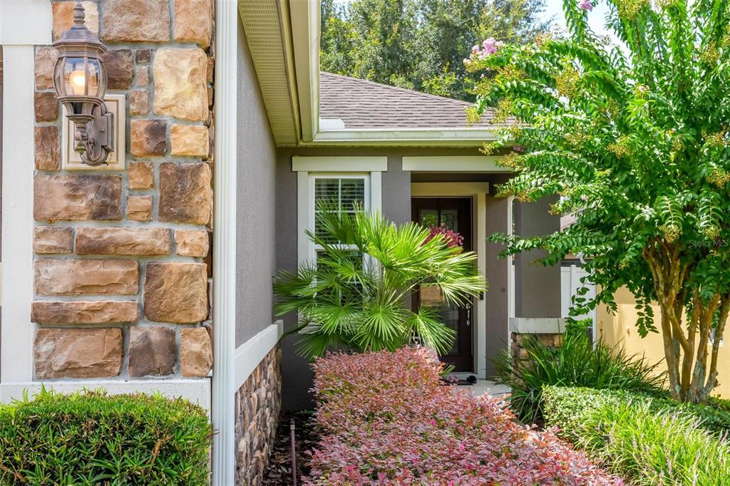 A stone-accented exterior wall with a lantern light leads to a front door and landscaping — 30539 LIPIZZAN TERRACE, MOUNT DORA, FL