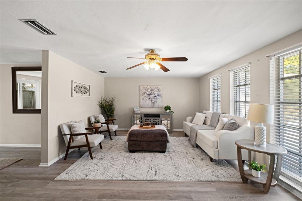 A living room features a brown sofa, a white media console with a fireplace, and wood-look flooring — 7710 BIRCHWOOD DRIVE, PORT RICHEY, FL