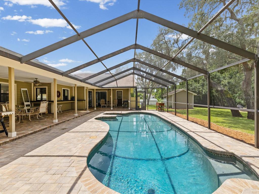 A screened-in swimming pool with a paver deck sits beside a house with a covered patio — 6655 MILLSTONE DRIVE, NEW PORT RICHEY, FL