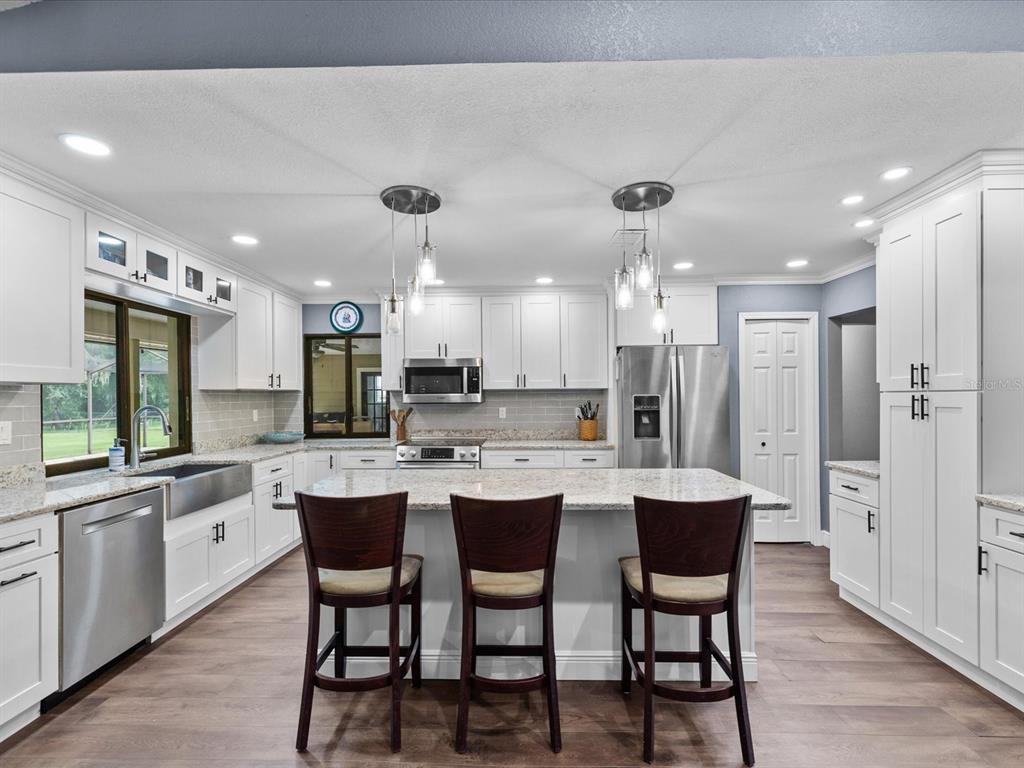 A modern kitchen features white cabinets, granite countertops, stainless steel appliances, and a central island — 6655 MILLSTONE DRIVE, NEW PORT RICHEY, FL