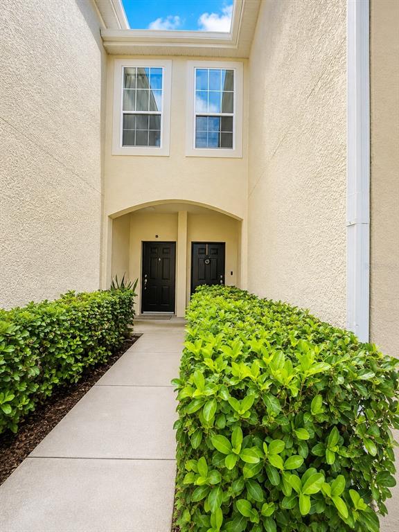 A concrete walkway leads to two black front doors recessed under a beige stucco archway — 351 VANGUARD POINT, CASSELBERRY, FL