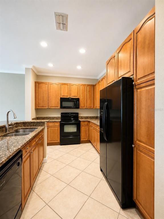 A kitchen with wood cabinets, granite countertops, black appliances, and diagonal tile flooring — 351 VANGUARD POINT, CASSELBERRY, FL