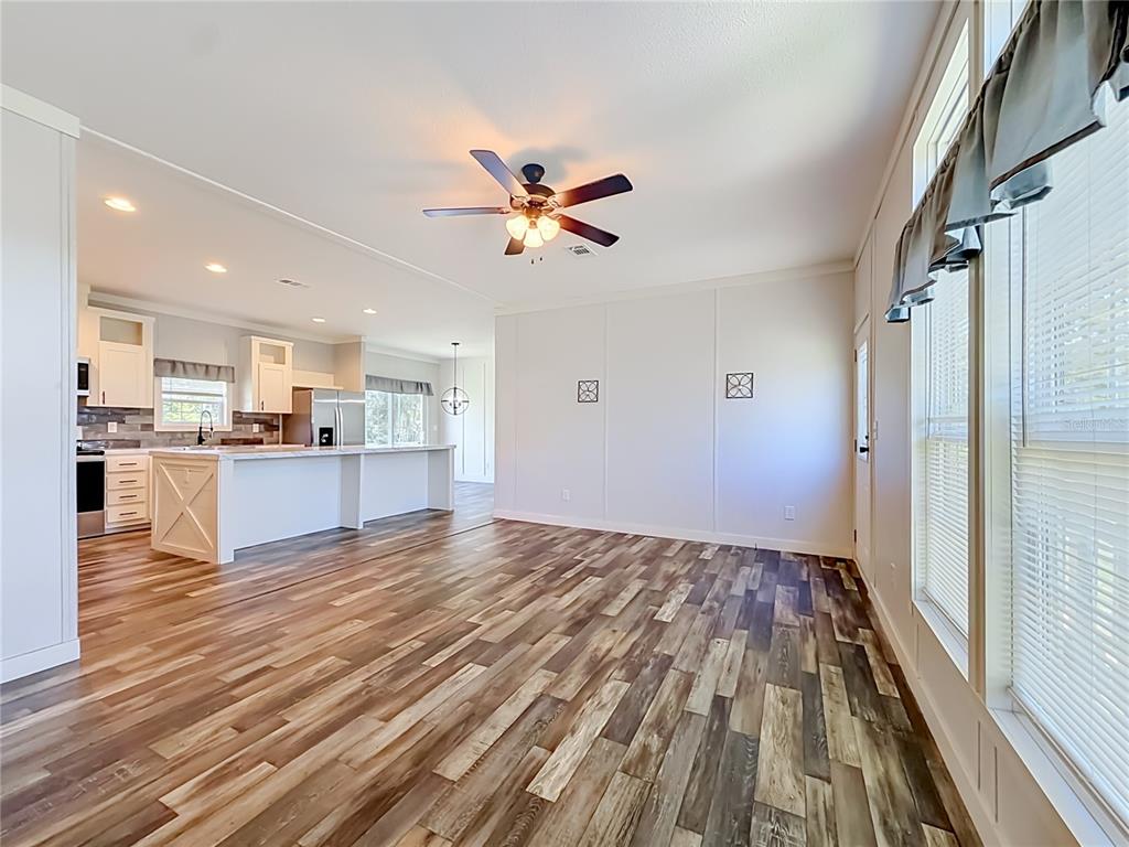 An open-concept living area with wood-look flooring, a ceiling fan, and an adjacent white kitchen — 5360 W CARAWAY PLACE, LECANTO, FL