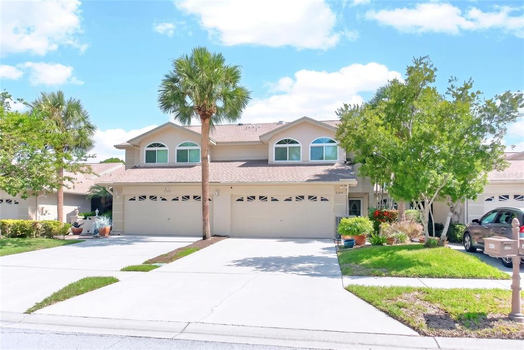 A two-story townhouse exterior features a beige facade, a two-car garage, and arched windows — 2524 W BROOK LANE, CLEARWATER, FL