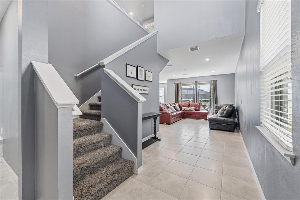 A carpeted staircase leads up from a tiled entryway into a living room with furniture — 5505 MISTY OAK CIRCLE, DAVENPORT, FL