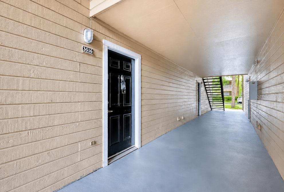 A covered outdoor walkway leads to a black front door with a house number sign — 1015 S HIAWASSEE ROAD UNIT 3516, ORLANDO, FL