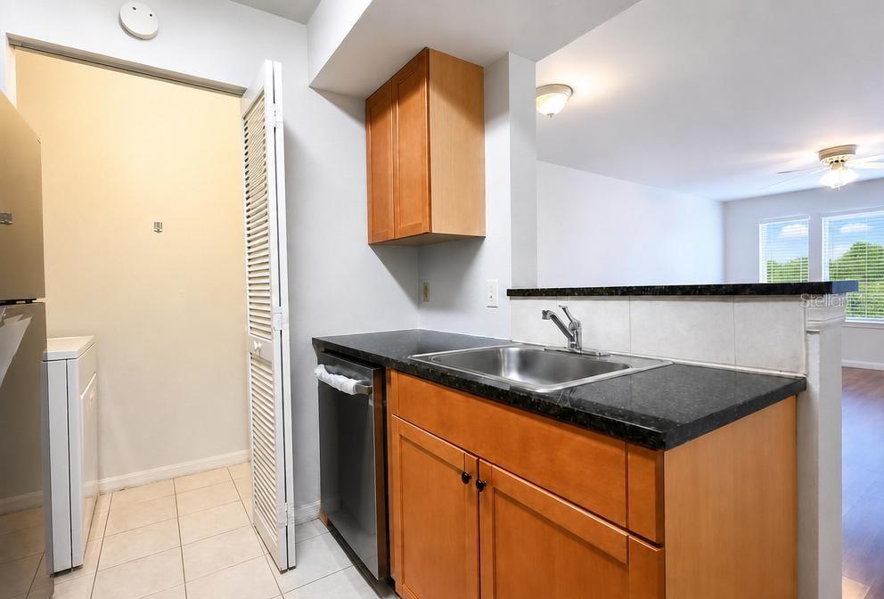 A kitchen features wood cabinets, dark countertops, a stainless steel dishwasher, and a laundry closet — 1015 S HIAWASSEE ROAD UNIT 3516, ORLANDO, FL