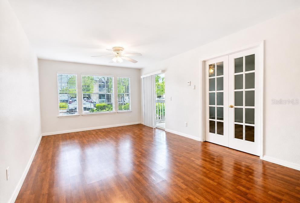 An empty living room features wood-look flooring, a ceiling fan, large windows, and French doors — 1015 S HIAWASSEE ROAD UNIT 3516, ORLANDO, FL