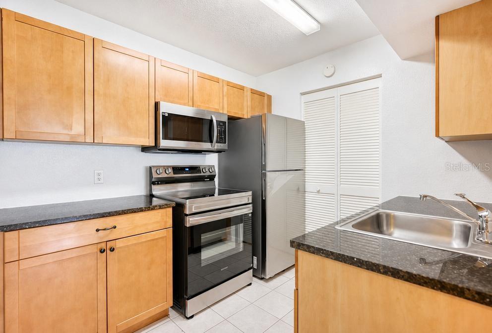 A kitchen features light wood cabinets, stainless steel appliances, and dark granite countertops — 1015 S HIAWASSEE ROAD UNIT 3516, ORLANDO, FL