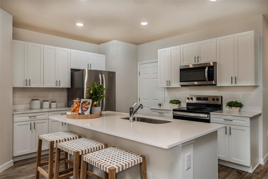 A modern kitchen features white cabinetry, stainless steel appliances, and a central island with seating — 9880 PELICAN COAST DRIVE, DADE CITY, FL