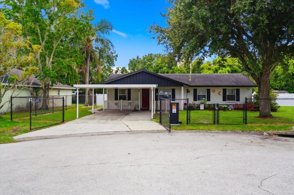 A single-story brick house features a carport, a white front porch railing, and a chain-link fence — 156 MANSEAU DRIVE, WINTER HAVEN, FL