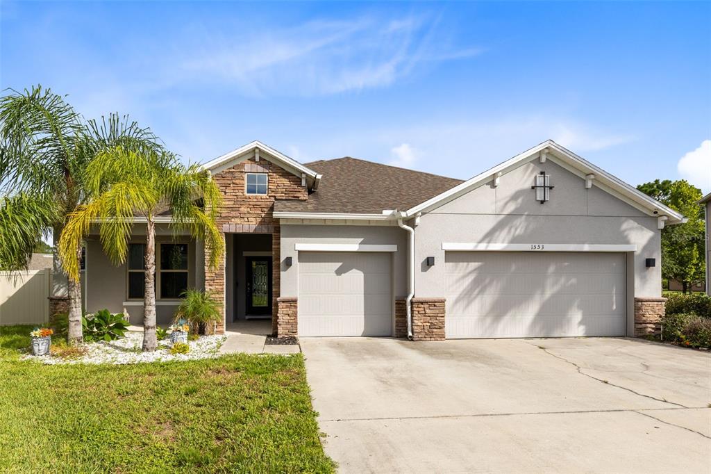A single-story house with a stone-accented facade, a three-car garage, and a palm tree — 1553 PINE MARSH LOOP, ST CLOUD, FL