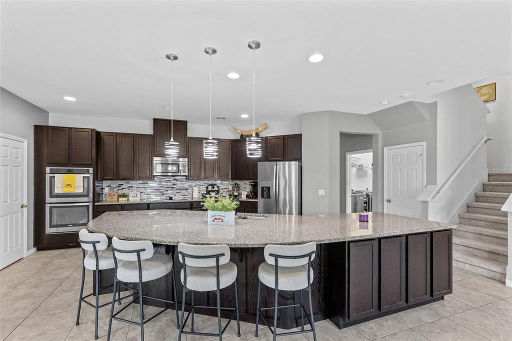 A kitchen features dark wood cabinets, a large curved granite island, and four bar stools — 1553 PINE MARSH LOOP, ST CLOUD, FL