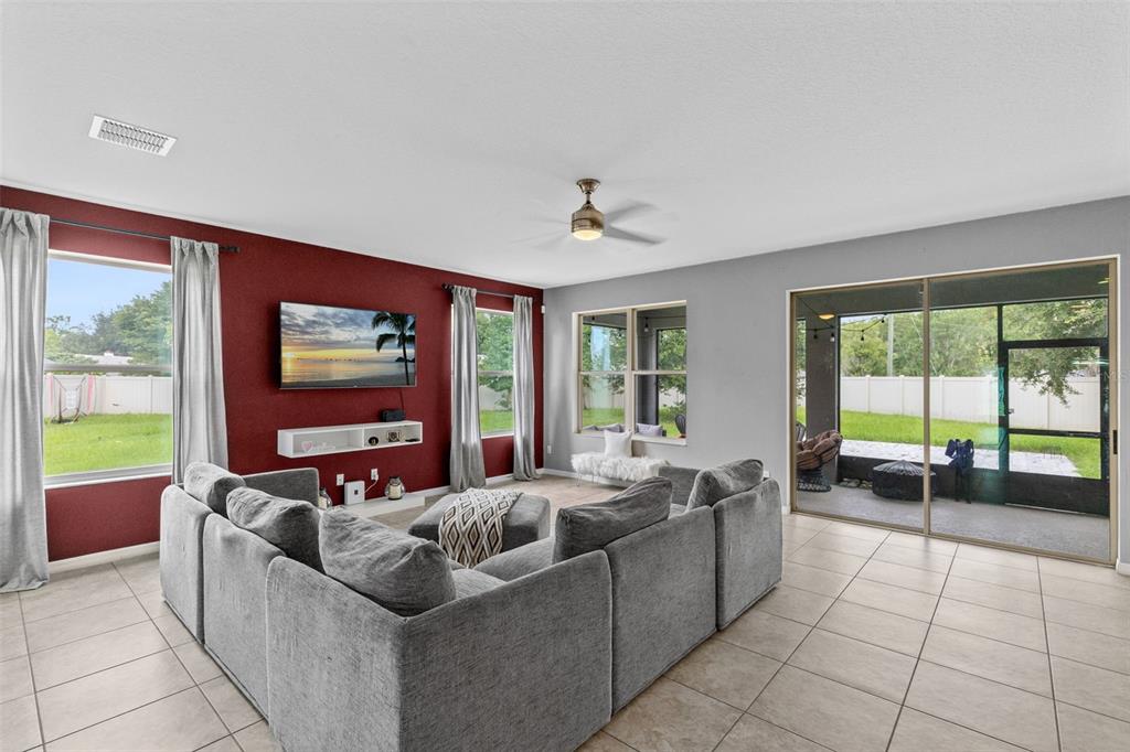 A living room features a red accent wall, gray sectional sofa, and sliding glass doors — 1553 PINE MARSH LOOP, ST CLOUD, FL