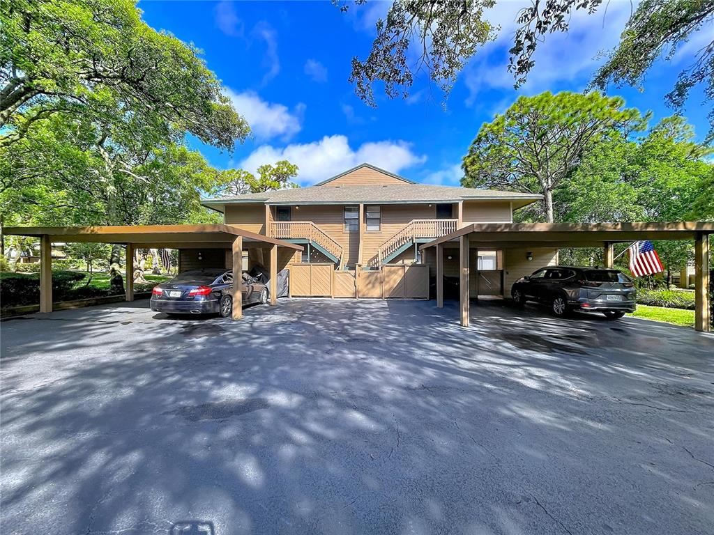 A two-story tan apartment building with a covered carport and a grassy lawn — 1006 LENNOX ROAD W UNIT 1006, PALM HARBOR, FL