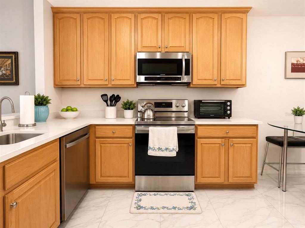 A kitchen features light wood cabinets, stainless steel appliances, white countertops, and white tile flooring — 9416 MYRTLE CREEK LANE UNIT 702, ORLANDO, FL