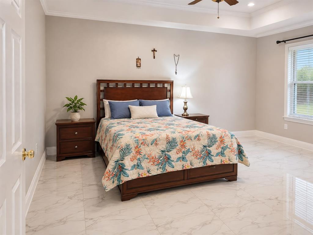 A bedroom features a wooden bed with a floral quilt, tile flooring, and neutral walls — 9416 MYRTLE CREEK LANE UNIT 702, ORLANDO, FL