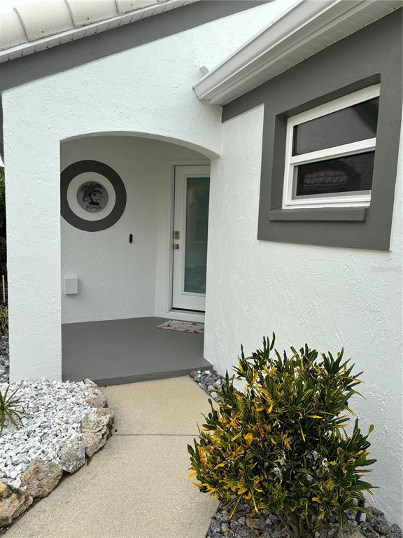 The exterior of a house features a white stucco facade, a gray-trimmed window, and a covered entryway — 1332 CAPRI ISLES BOULEVARD, VENICE, FL