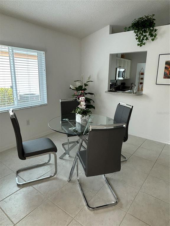 A dining area features a glass-topped table, four modern chairs, and a kitchen pass-through window — 1332 CAPRI ISLES BOULEVARD, VENICE, FL