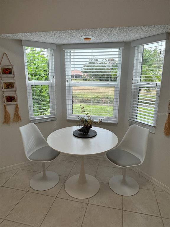 A breakfast nook features a white pedestal table, two modern chairs, and three bay windows — 1332 CAPRI ISLES BOULEVARD, VENICE, FL