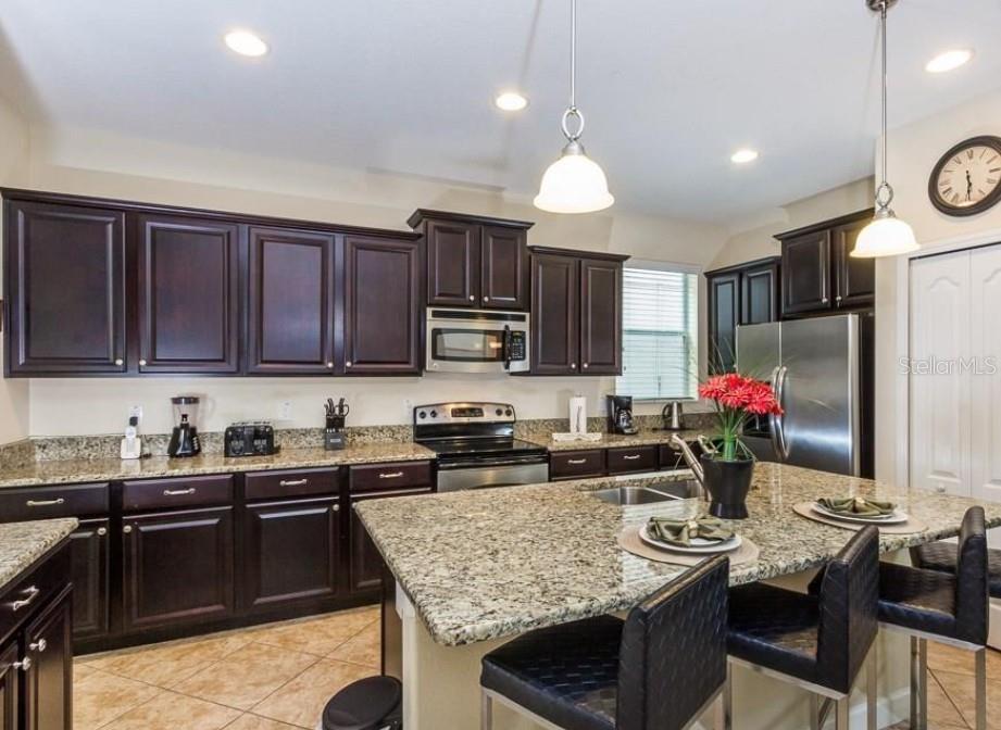 A kitchen with dark wood cabinets, granite countertops, a center island, and stainless steel appliances — 8935 CUBAN PALM ROAD, KISSIMMEE, FL