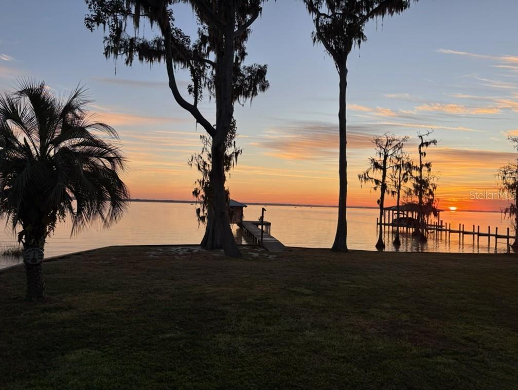 A sunset view over a lake featuring a grassy lawn, palm tree, and two wooden docks — 108 SANDRA LANE, CRESCENT CITY, FL