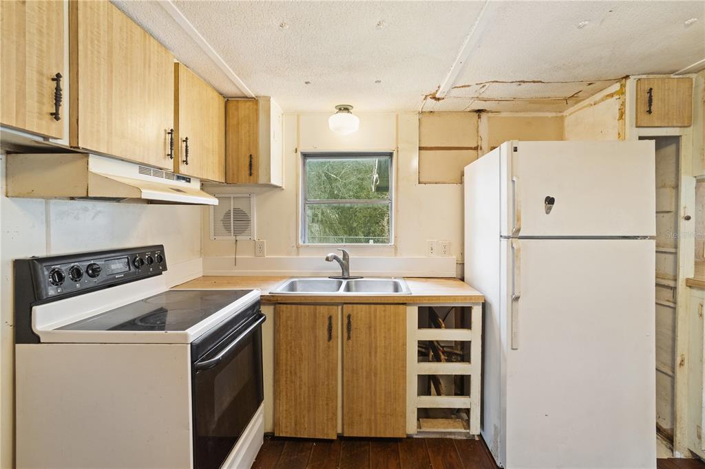 A kitchen features wood-look cabinets, a white stove, a refrigerator, and a double basin sink — 108 CHERYL ELAINE DRIVE, BUNNELL, FL