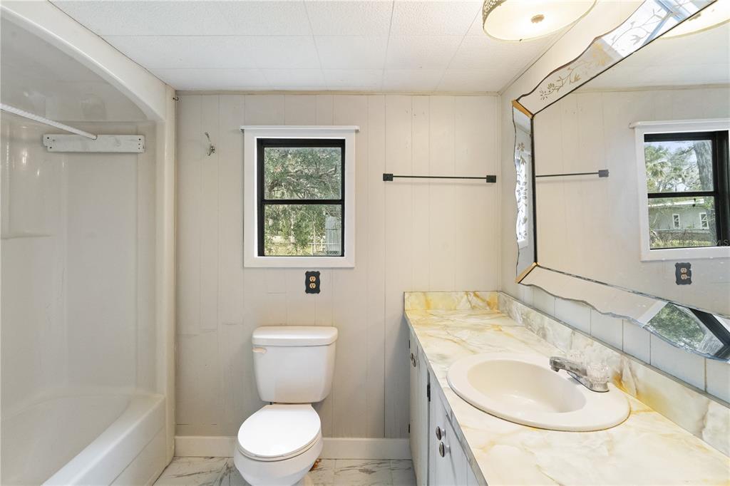 A bathroom features a shower-tub combo, a toilet, and a vanity with a marble-patterned countertop — 108 CHERYL ELAINE DRIVE, BUNNELL, FL