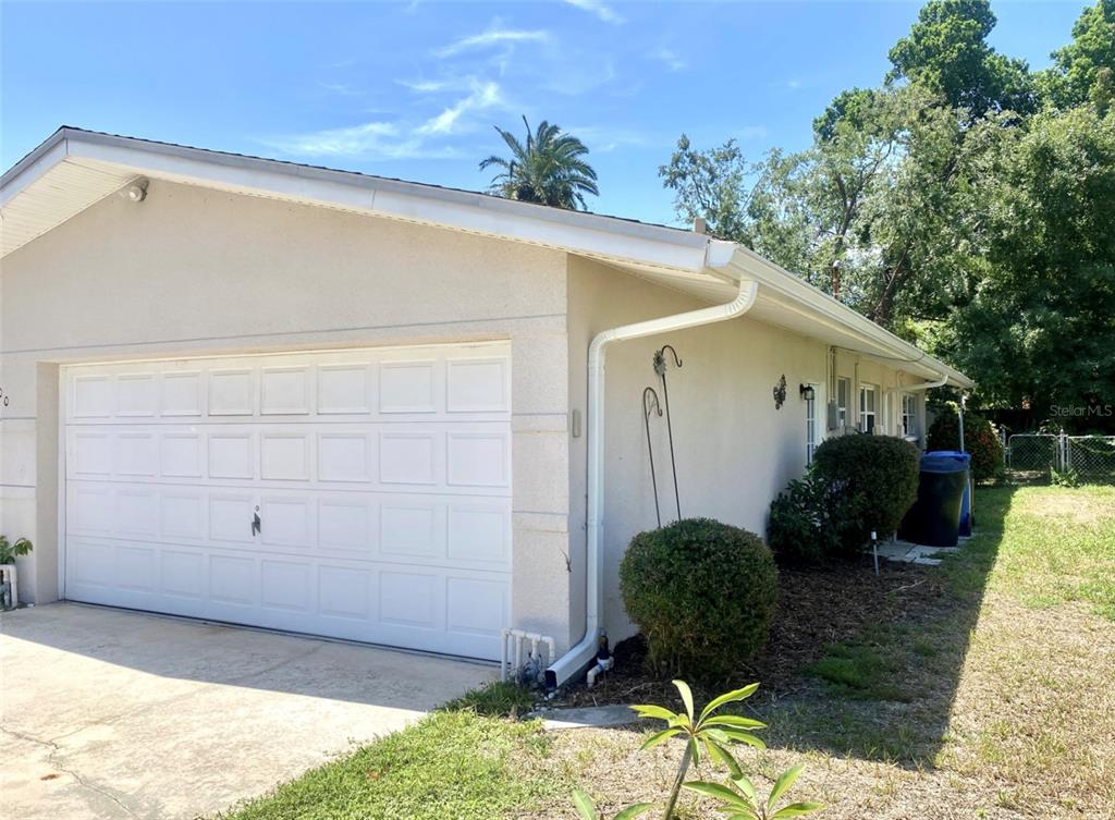 A side view of a house exterior featuring a white garage door and beige stucco walls — 100 59TH AVENUE S, ST PETERSBURG, FL