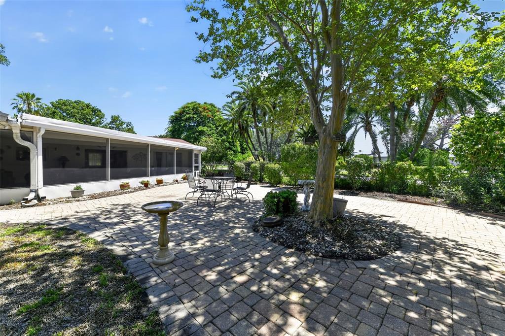 A paved patio features a large tree, a birdbath, and a screened-in porch area — 100 59TH AVENUE S, ST PETERSBURG, FL