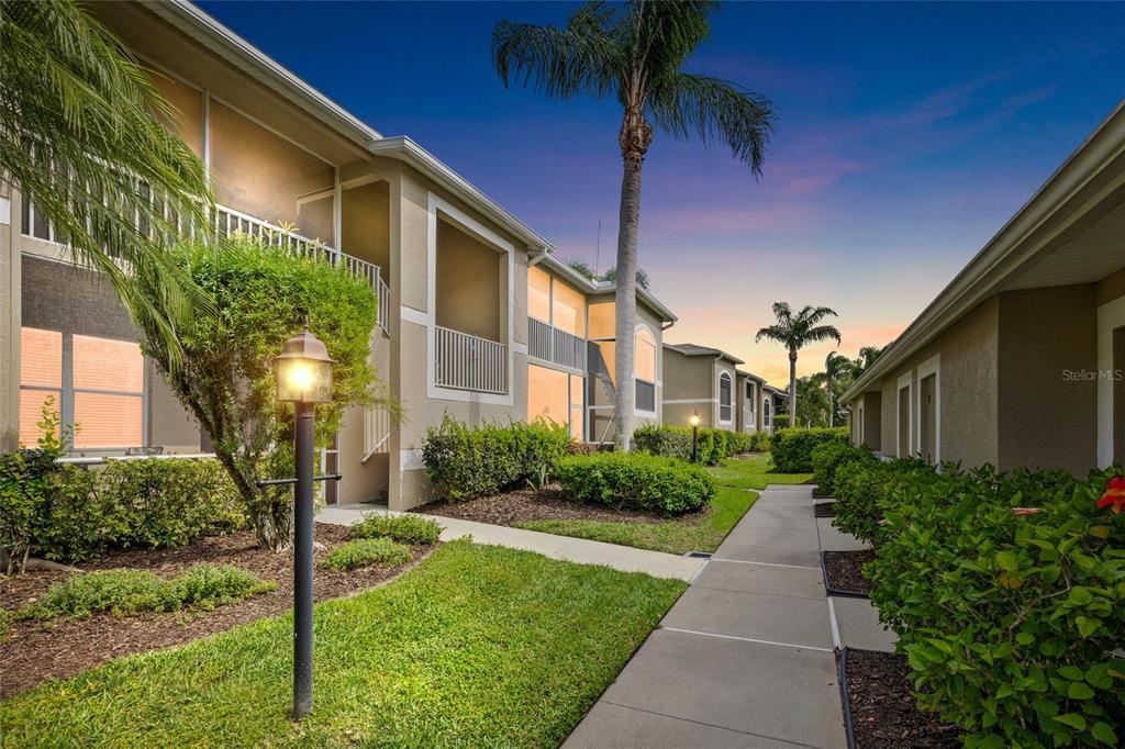 A two-story apartment building exterior features a screened-in entryway, white railings, and landscaped bushes — 5231 MAHOGANY RUN AVENUE UNIT 325, SARASOTA, FL