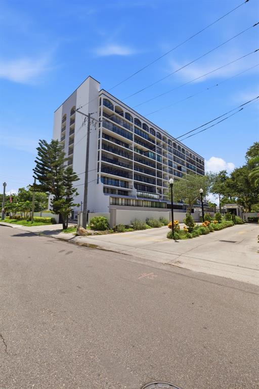 A multi-story residential apartment building stands behind a concrete driveway and landscaped garden area — 3211 W SWANN AVENUE UNIT 1103, TAMPA, FL