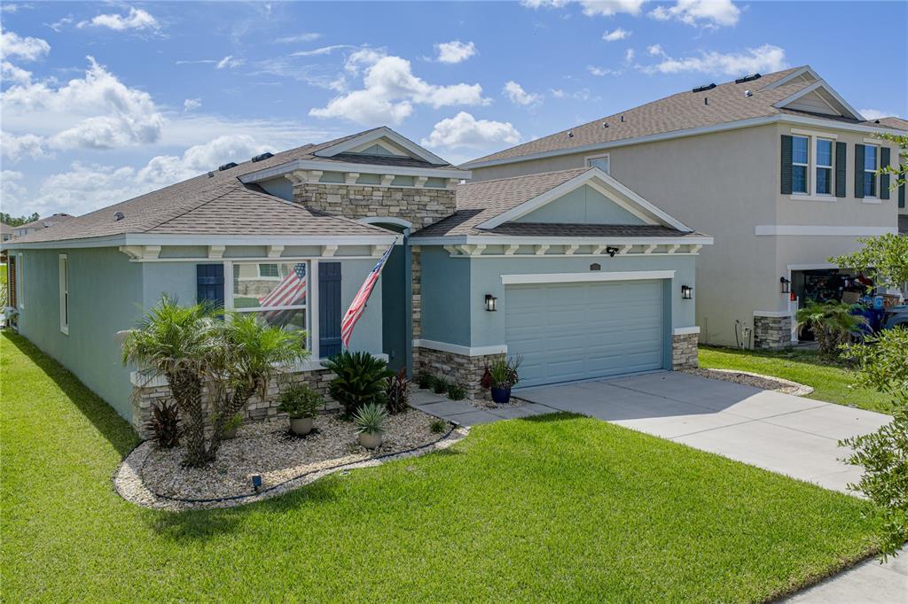 A single-story house with blue siding, stone accents, a two-car garage, and a landscaped yard — 8382 BOWER BASS CIRCLE, WESLEY CHAPEL, FL