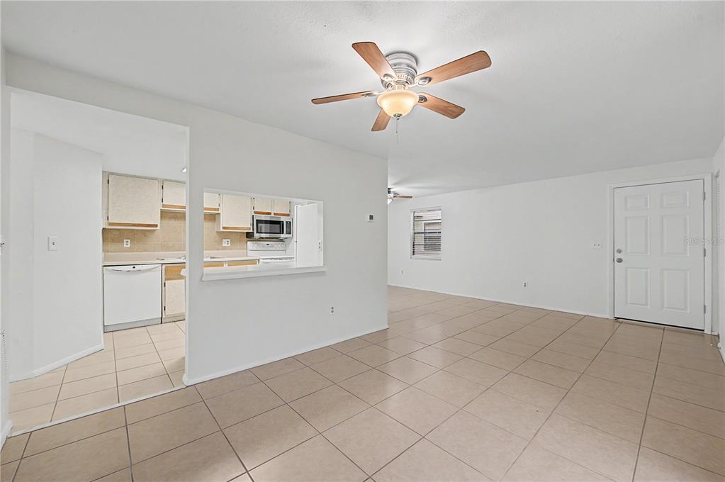 An interior view shows a living area with tile floors, a ceiling fan, and kitchen pass-through — 123 LOBLOLLY COURT UNIT A, OLDSMAR, FL