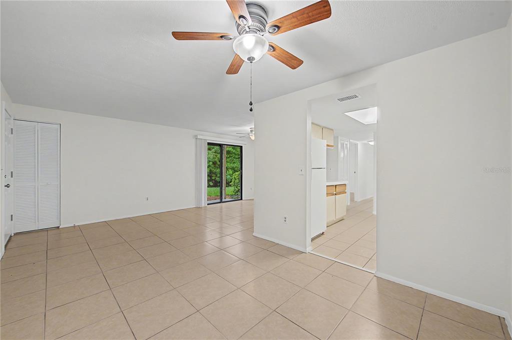 A tiled living room features a ceiling fan, sliding glass doors, and an adjacent kitchen — 123 LOBLOLLY COURT UNIT A, OLDSMAR, FL
