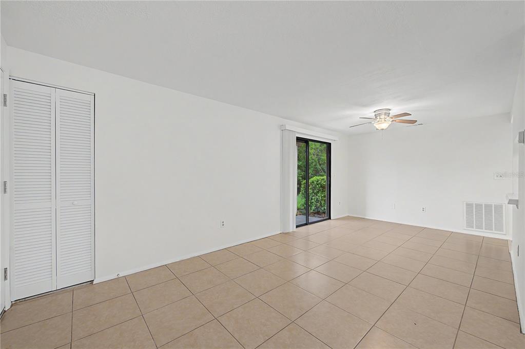 An empty room with white walls, tile flooring, a ceiling fan, and a sliding glass door — 123 LOBLOLLY COURT UNIT A, OLDSMAR, FL