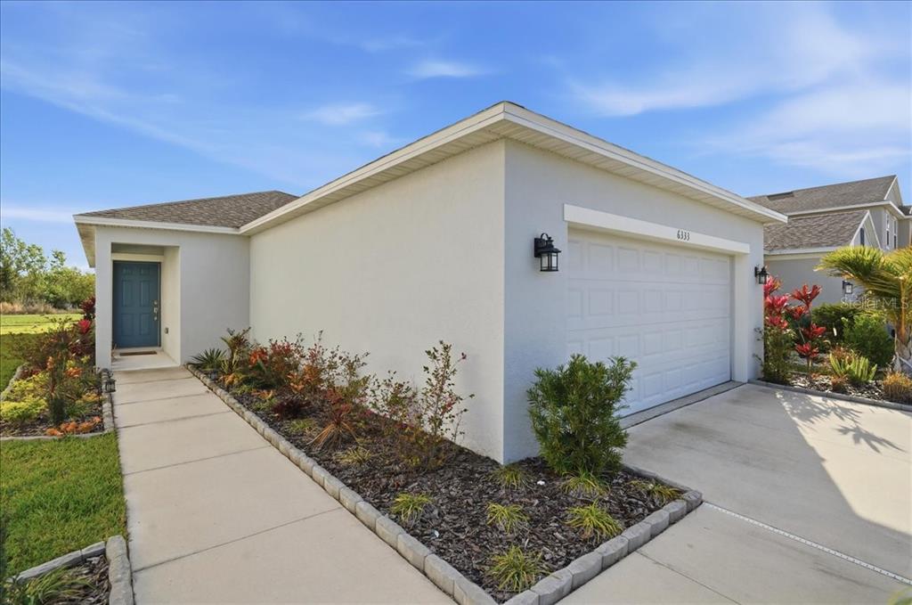 A single-story house exterior features a light-colored stucco facade, a garage, and a concrete walkway — 6333 MILESTONE LOOP, PALMETTO, FL
