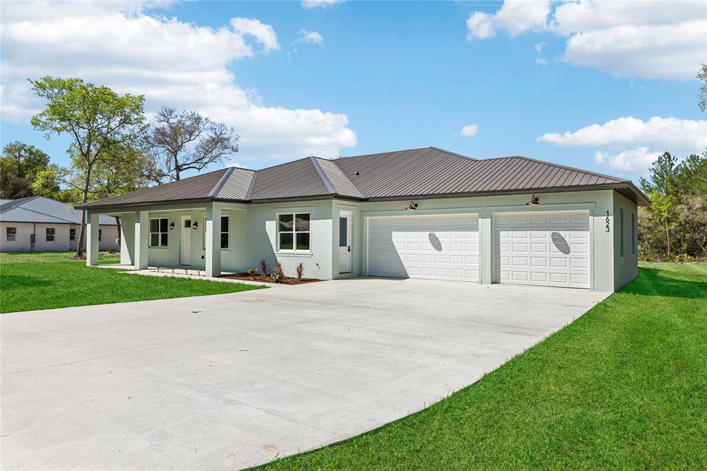 A single-story house with a metal roof, light-colored stucco exterior, and a two-car garage — 351 MITNIK DRIVE, DELTONA, FL