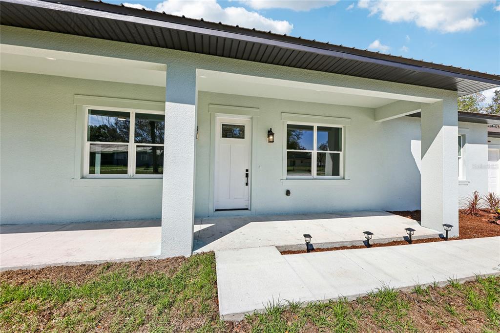 A light green house exterior features a covered front porch, white door, and concrete walkway — 351 MITNIK DRIVE, DELTONA, FL