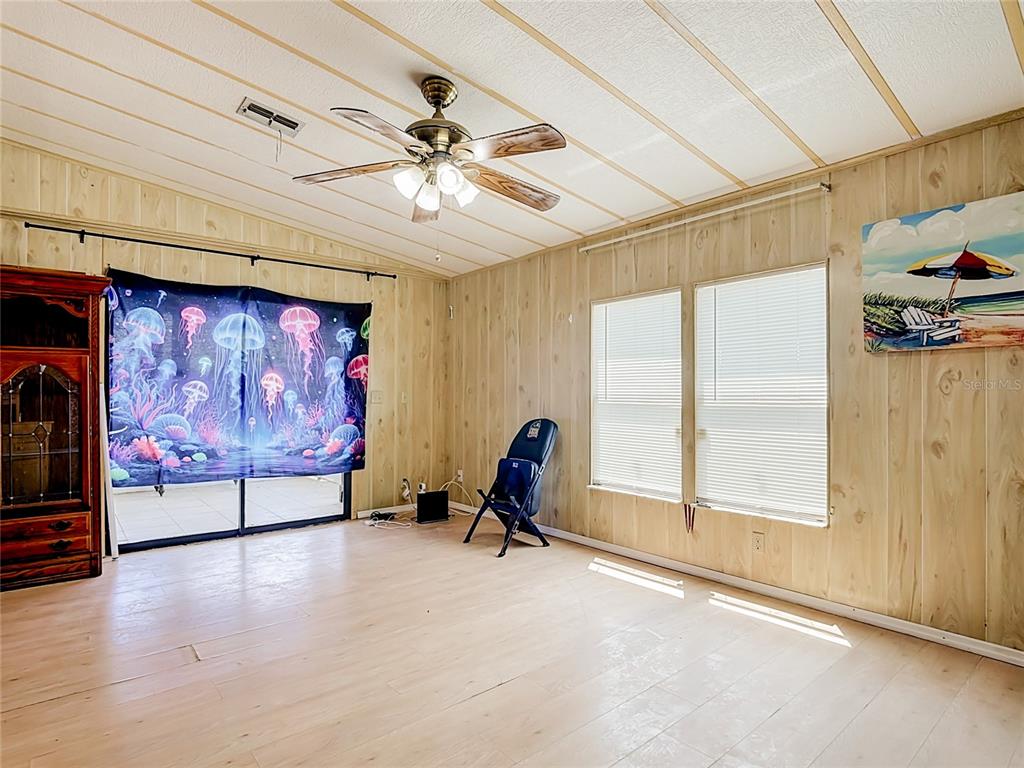 A living room features wood-paneled walls, light-colored flooring, a ceiling fan, and a jellyfish tapestry — 2614 MC DANIEL DRIVE, KISSIMMEE, FL