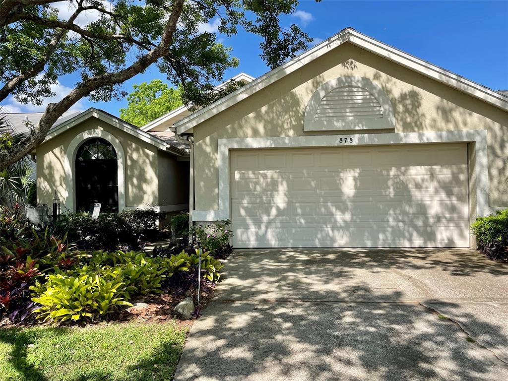 A single-story house with a beige stucco exterior, a two-car garage, and landscaped front yard — 878 E CHARING CROSS CIRCLE, LAKE MARY, FL