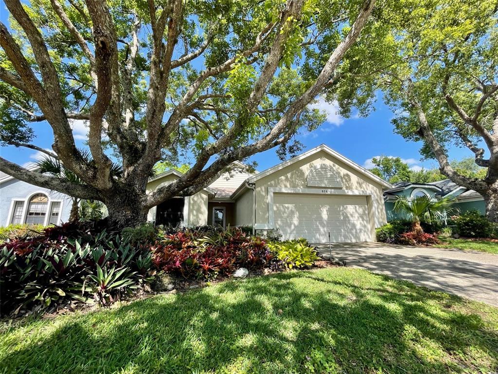 A single-story house with a two-car garage, a large tree, and landscaped garden beds — 878 E CHARING CROSS CIRCLE, LAKE MARY, FL