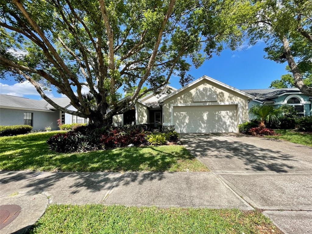 A single-story house with a two-car garage, a large tree, and landscaping in the front yard — 878 E CHARING CROSS CIRCLE, LAKE MARY, FL