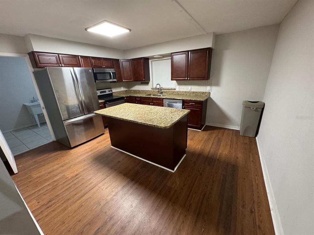 A kitchen features dark wood cabinets, granite countertops, a center island, and wood-look flooring — 2211 SUNNY VIEW DR, OVIEDO, FL