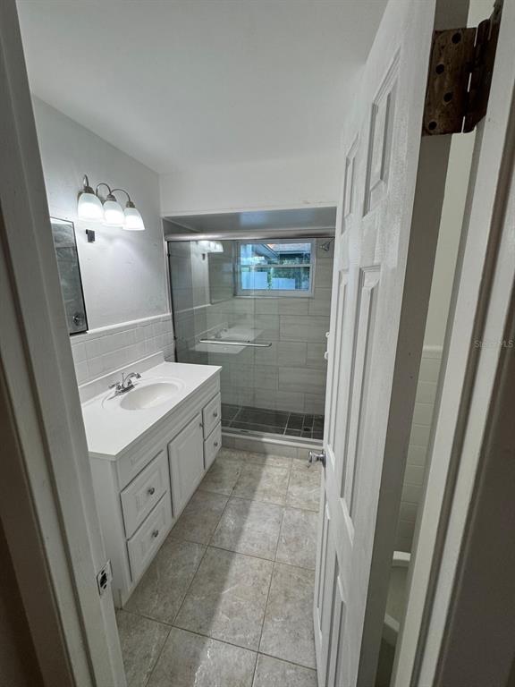 A bathroom featuring a white vanity, a glass-enclosed shower, and light-colored tile flooring — 2211 SUNNY VIEW DR, OVIEDO, FL