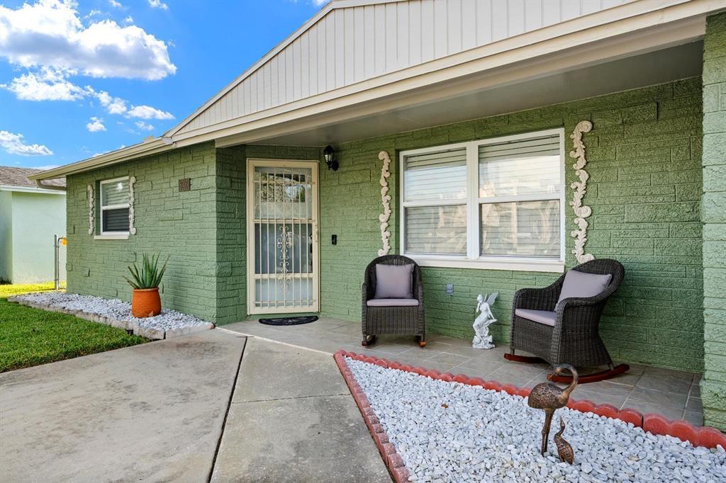 A green brick house exterior features a porch with two wicker rocking chairs and landscaping — 8505 OLD POST ROAD, PORT RICHEY, FL