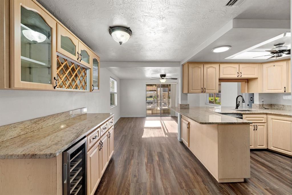 A kitchen with light wood cabinets, granite countertops, and wood-look flooring leads to a dining area — 8505 OLD POST ROAD, PORT RICHEY, FL