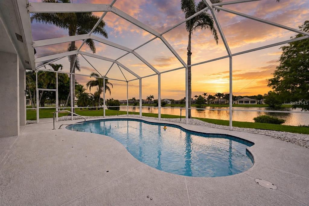 A screened-in swimming pool overlooks a lake at sunset with palm trees in the background — 468 SW TALQUIN LANE, PORT ST LUCIE, FL